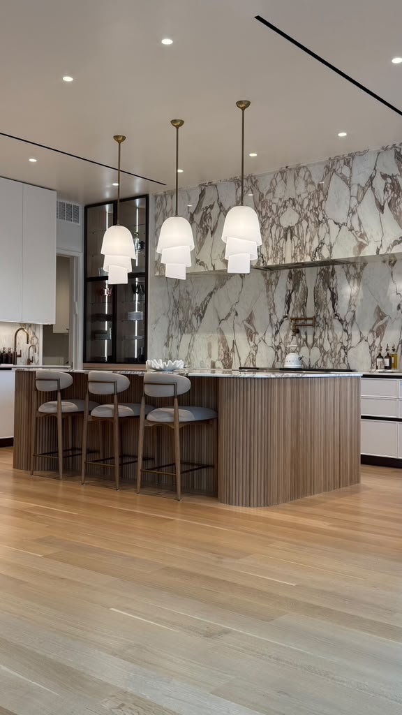 Kitchen with marble-clad wall, ribbed wood island, and blown-glass dome pendants